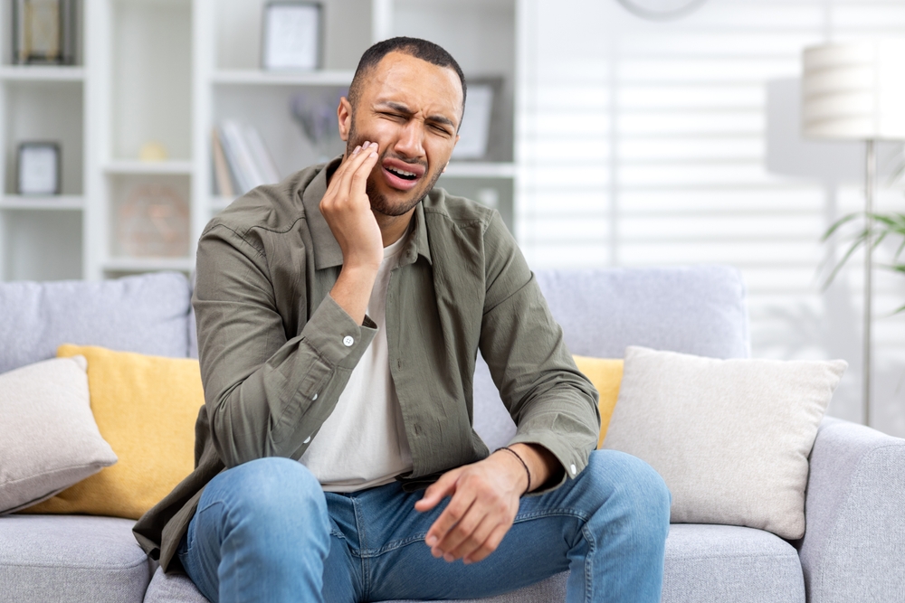 Man holding his cheek while seated on a sofa at home